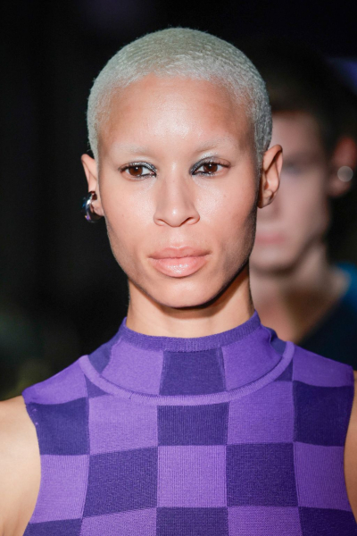 A model with short bleached hair wearing a sleeveless purple checkered top